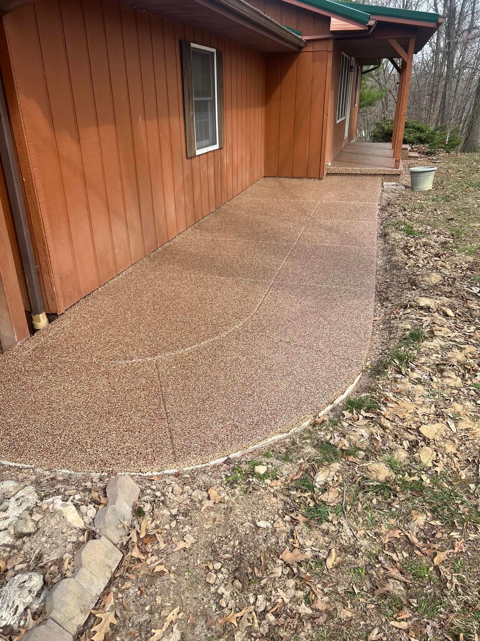 Pebble walkway beside a brown wooden house, curving past a small porch.