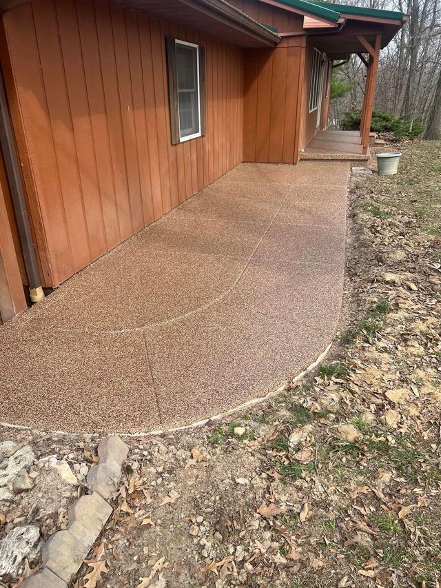Pebble walkway beside a brown wooden house, curving to a covered porch and garden bed.