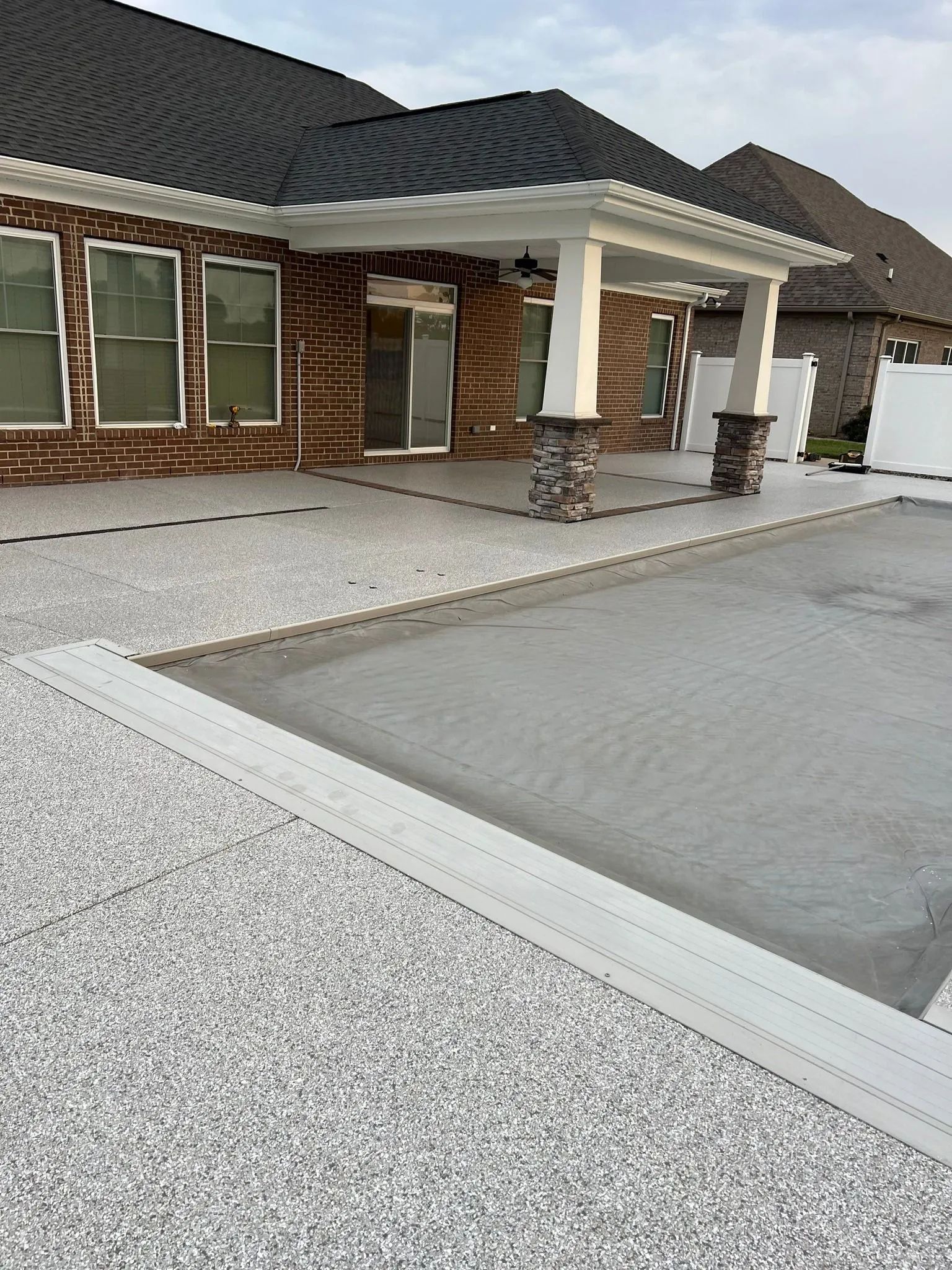Modern brick house exterior with white columns, dark roof, and a gravel driveway under construction