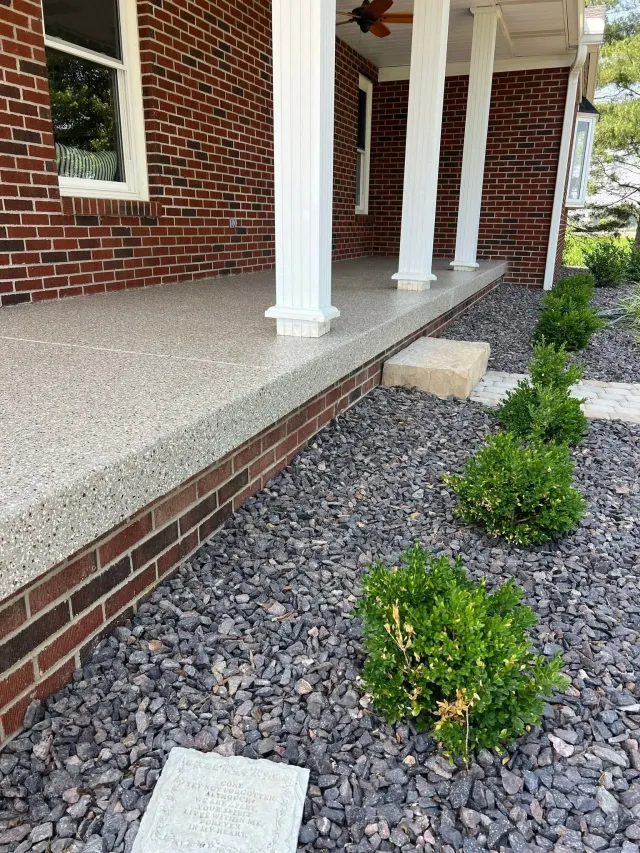Brick house porch with white columns and a gravel path lined with small shrubs