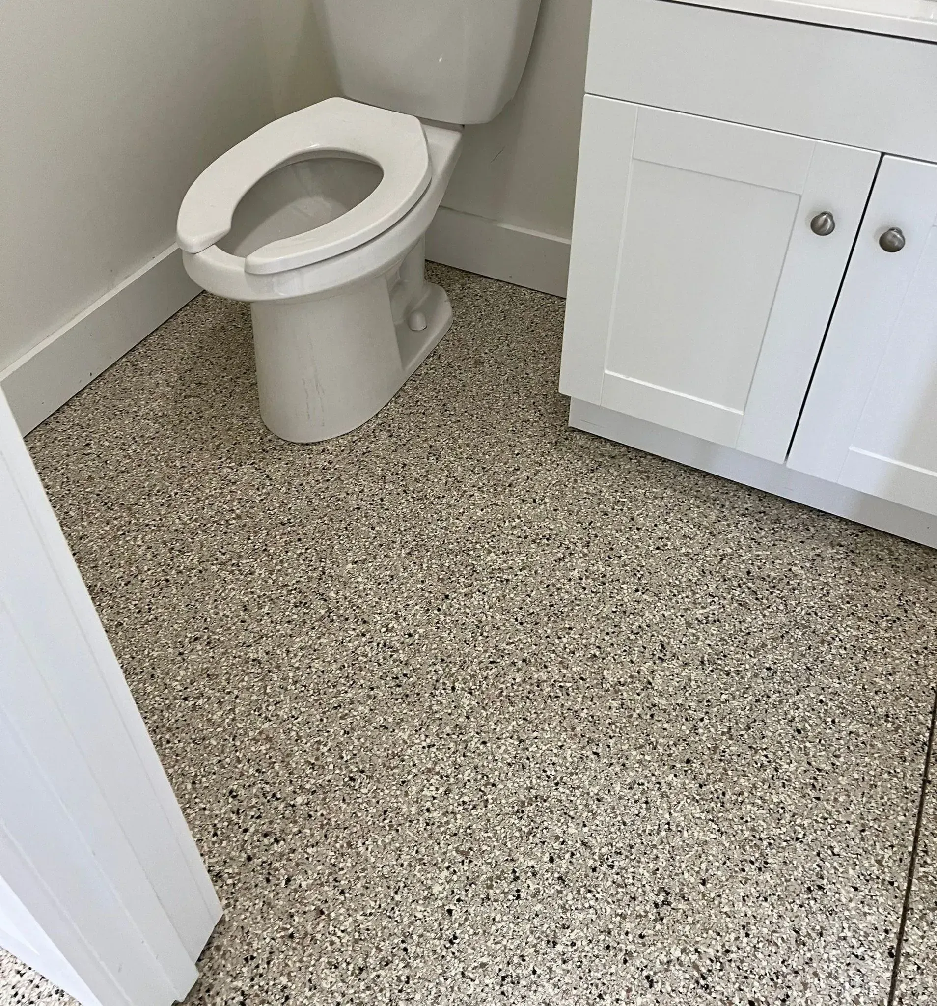 Small bathroom with a toilet and white cabinet on a speckled gray floor.