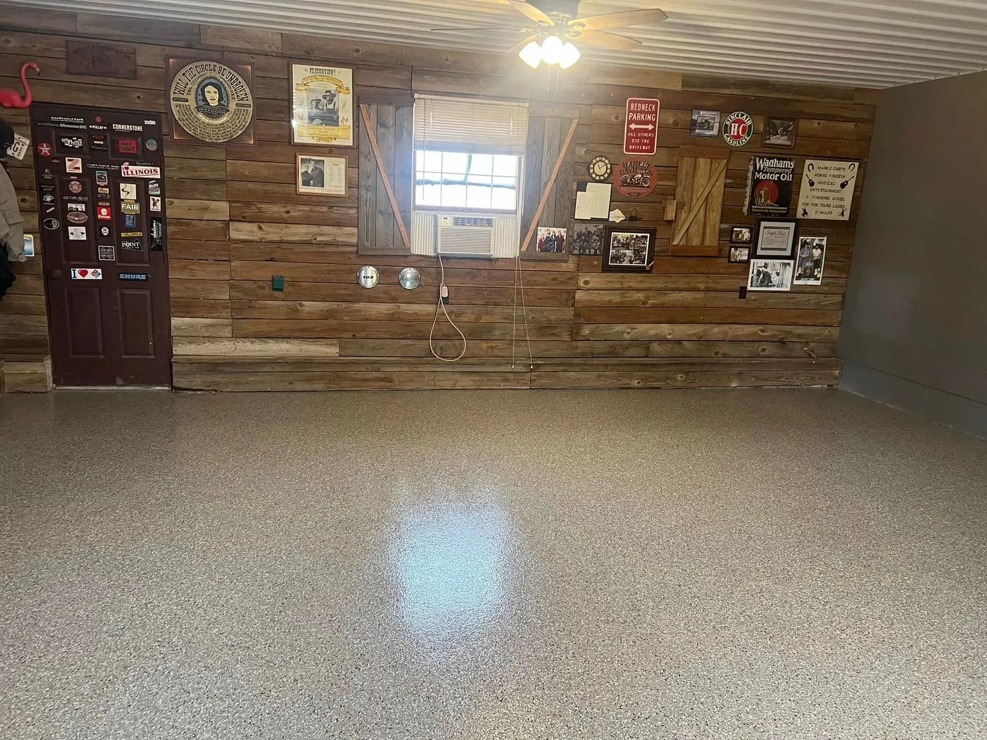 Empty room with wood-paneled wall, display shelves, wall decor, and a speckled floor under a window.