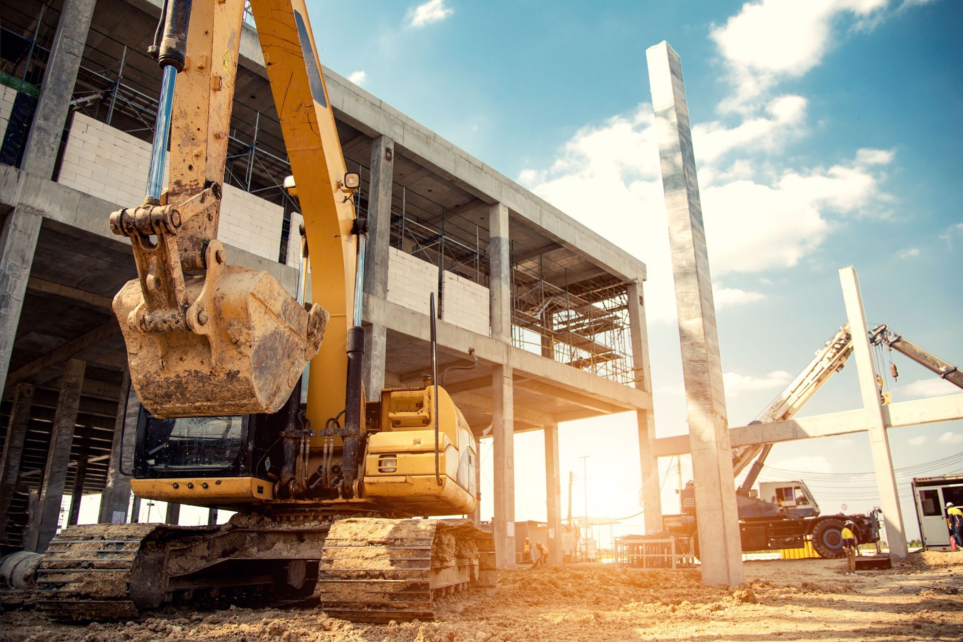 Construction site with excavator beside a concrete building under construction at sunset