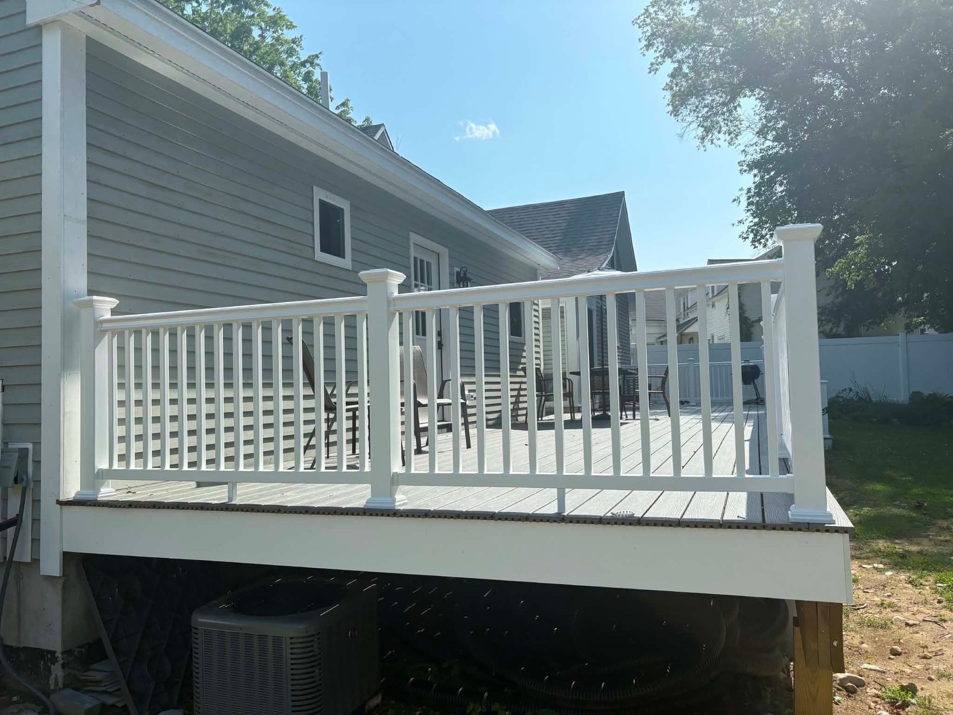 White backyard deck with railings attached to a gray house on a sunny day