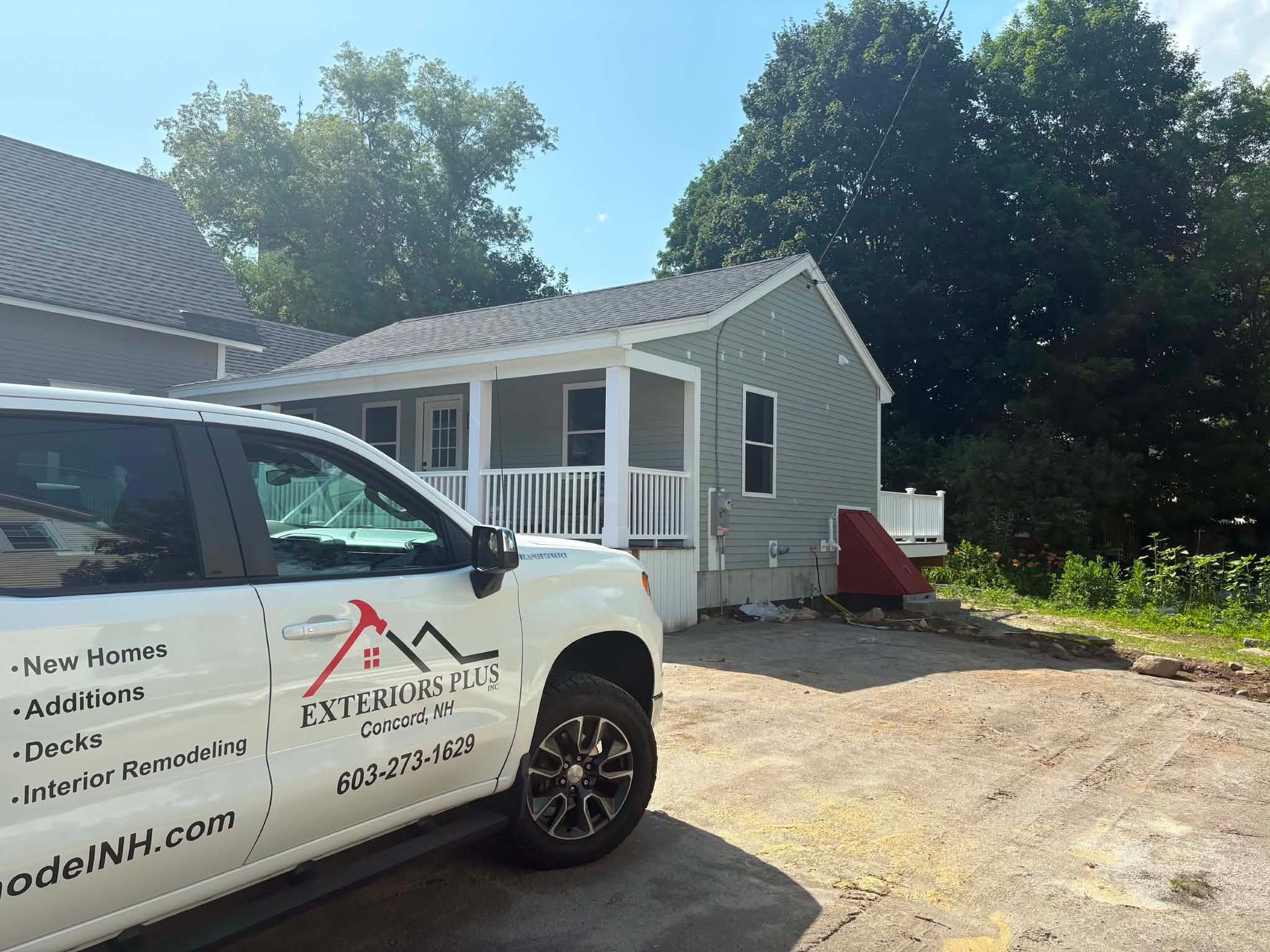 White work van in front of a small gray house with a gravel driveway and trees nearby.