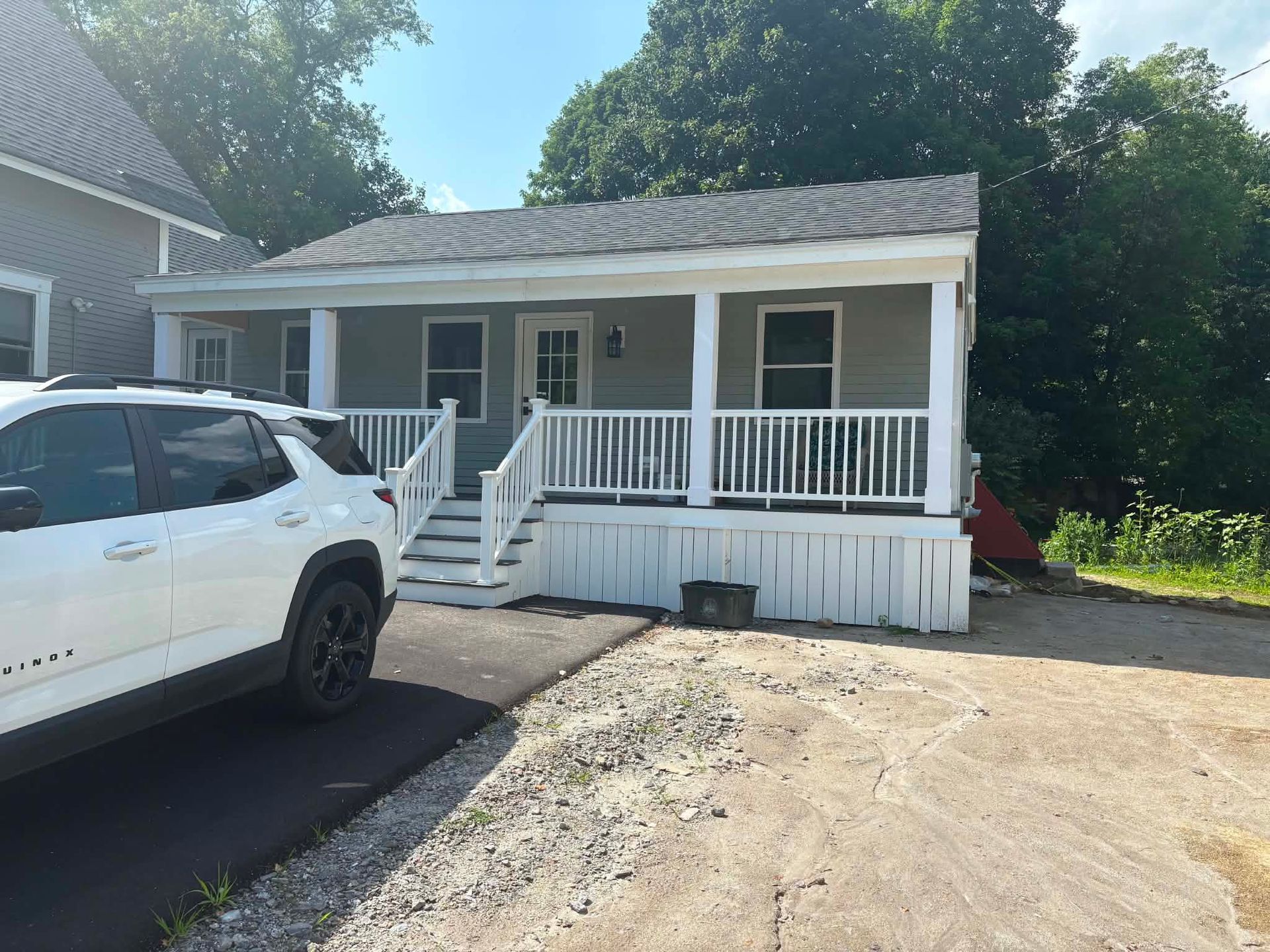 White house with front porch and stairs, partially blocked by a white SUV on a gravel driveway