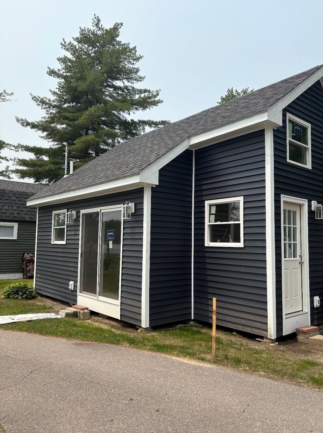 Dark blue cottage-style building with white trim, sliding glass doors, and a tree in the background