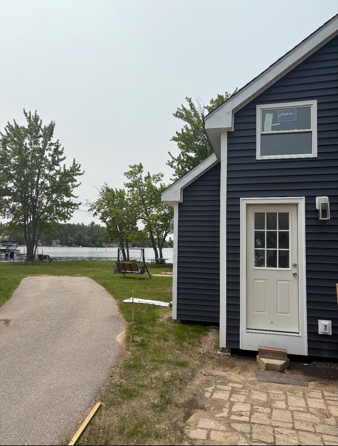 Blue house with white door beside a curved gravel drive and trees near water