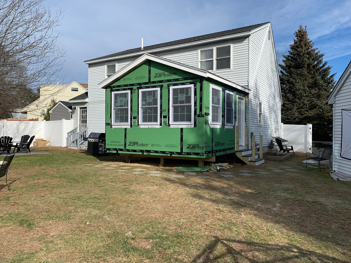 A small green house is being built in the backyard of a house.