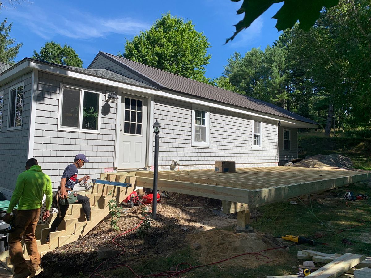 A group of people are working on a deck in front of a house.