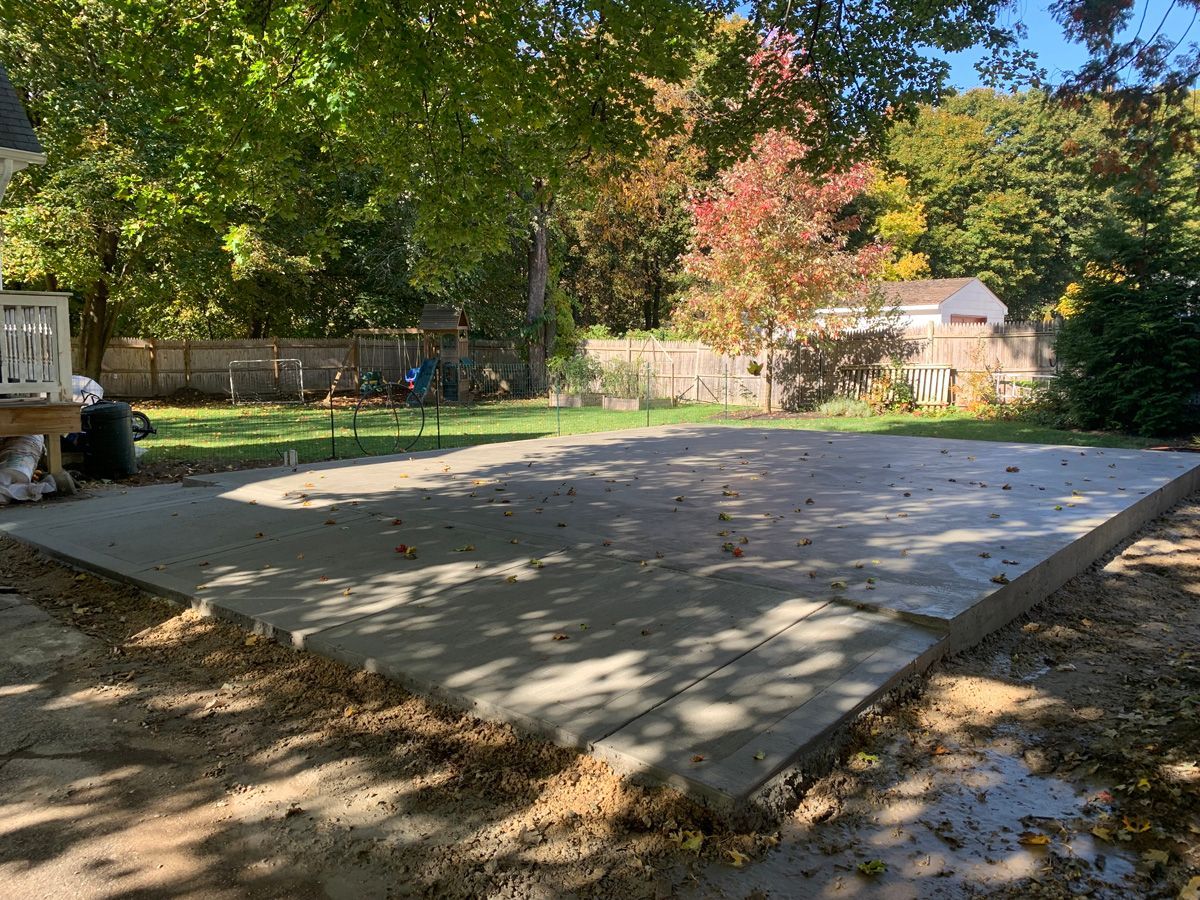 A concrete patio is being built in the backyard of a house.