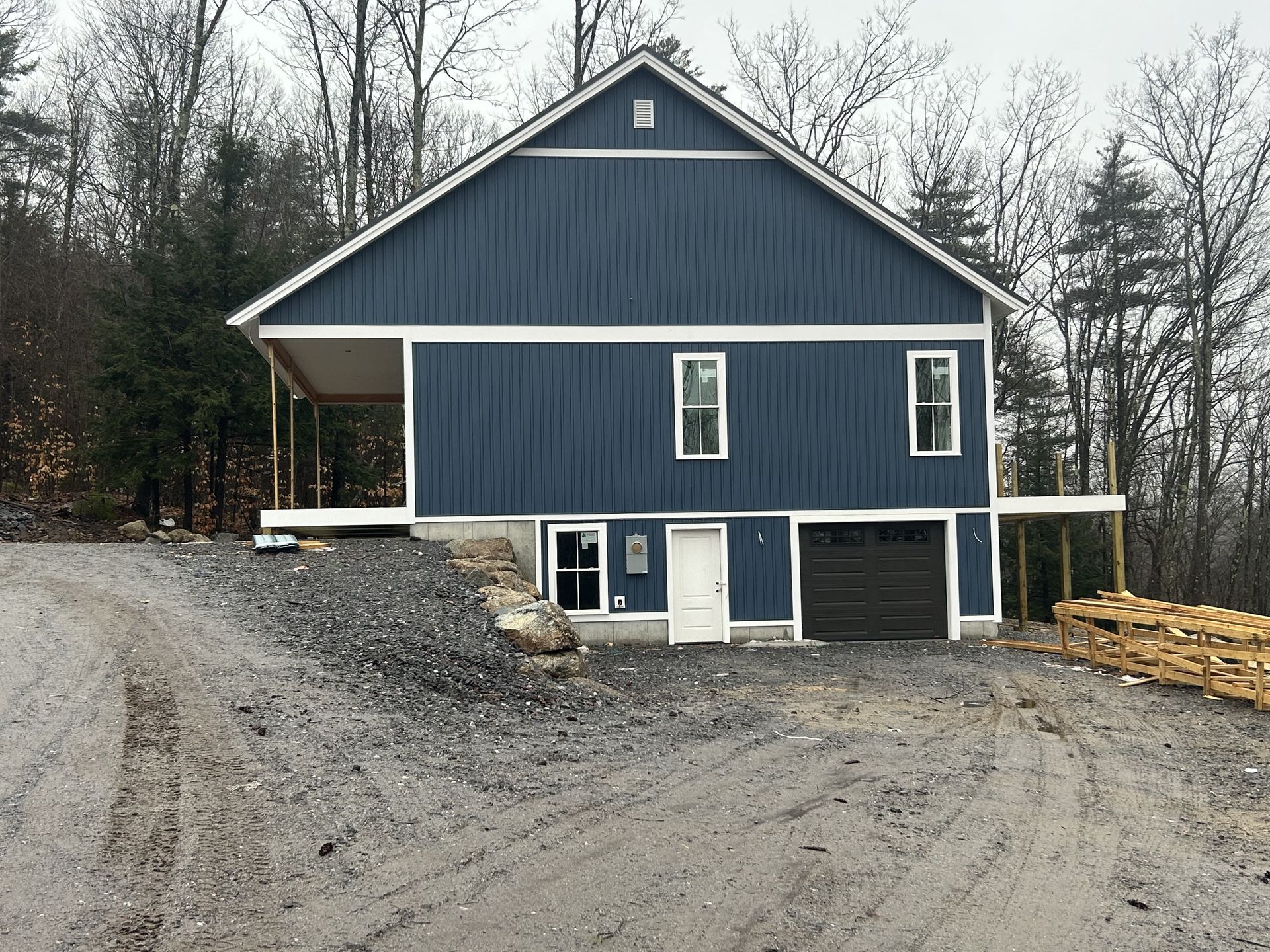 A blue house with a garage and porch is sitting on top of a dirt hill.
