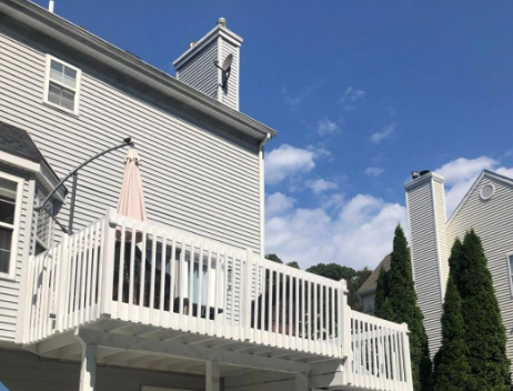 White deck and gray house exterior with umbrella under a blue sky