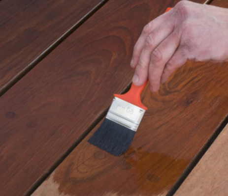 Hand holding a paintbrush, applying finish to a wooden surface.