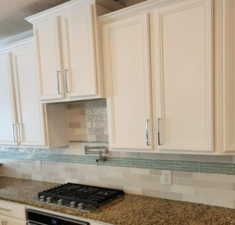 Cream kitchen cabinets above a granite countertop with a tiled backsplash and built-in stove area