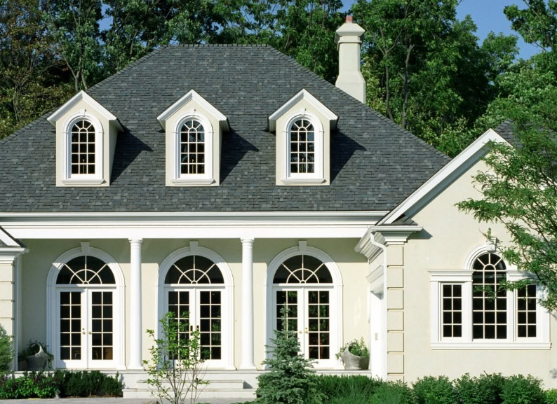 Cream-colored house with dark gray roof, white dormer windows, and a front porch with arched windows