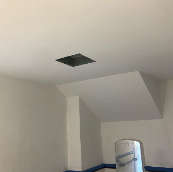 White room ceiling with a square recessed opening and a partially visible refrigerator below.