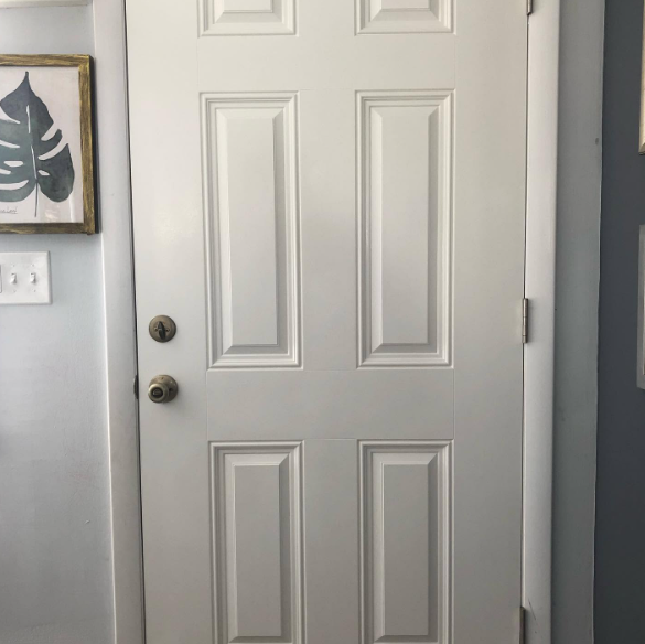 White front door with two panels and a dark round doorknob in a gray-walled entryway.