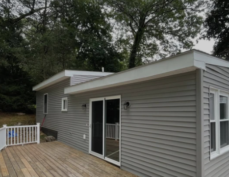 Gray house exterior with sliding glass doors and a wooden deck surrounded by trees