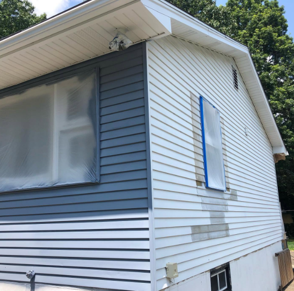 Two-story house exterior with white siding, gray upper wall, and blue shutters; windows are covered in plastic.