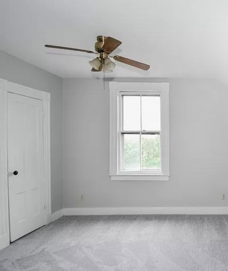 Empty gray bedroom with white closet, window, and ceiling fan on a carpeted floor.