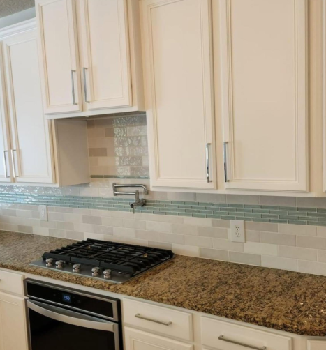 Modern kitchen with cream cabinets, granite countertop, gas range, and blue tile backsplash