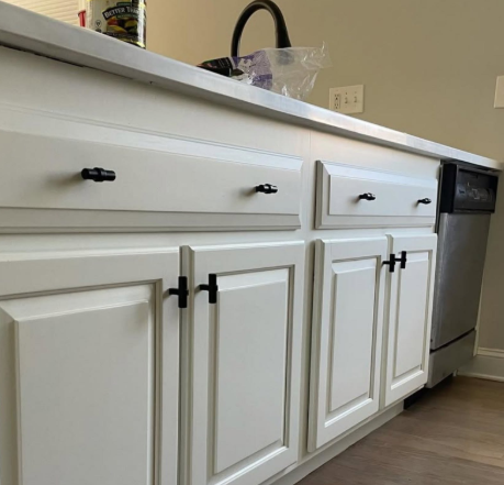 White kitchen cabinets and black dishwasher beneath a light countertop, seen from a low angle.