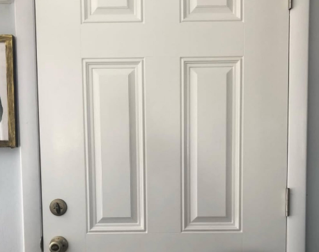 White front door with raised panels and a round doorknob, viewed indoors