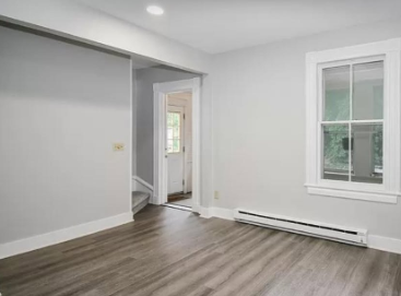 Empty white room with gray wood floors, a closet, door, and two windows.