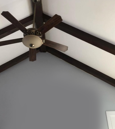 Ceiling fan with dark blades on a vaulted ceiling with exposed dark beams.