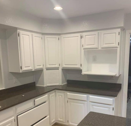 Small white kitchen with dark countertops, upper cabinets, and a built-in desk nook.