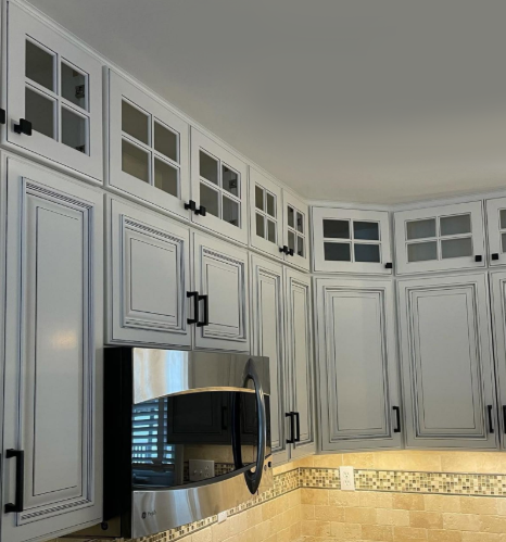 White kitchen cabinets with glass-front uppers, a stainless steel fridge, and beige tile backsplash under a curved ceiling