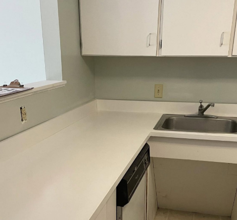 Empty office kitchenette with white counters, sink, and beige cabinets.
