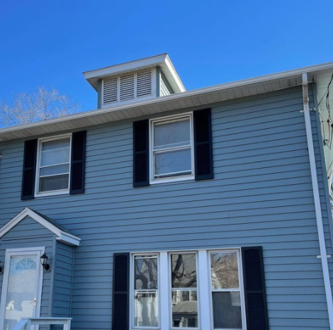 Blue two-story house with black shutters and a small dormer against a clear sky