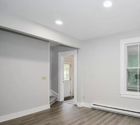 Empty gray room with wood floors, recessed lights, and a doorway leading to stairs