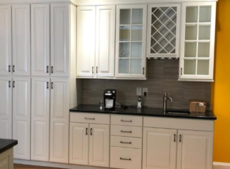 White kitchen cabinets with black countertop, sink, coffee maker, and wine rack backsplash