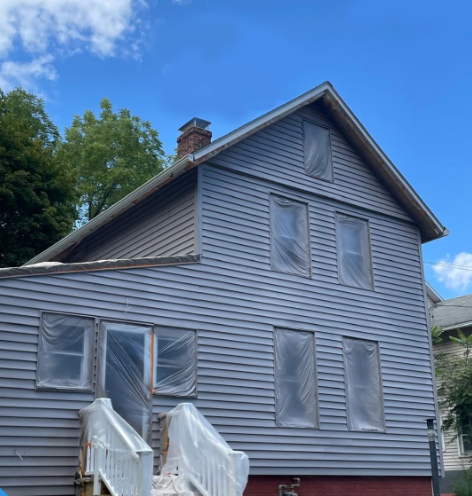 Gray house with boarded windows and front steps against a blue sky