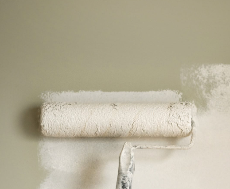 Paint roller applying white paint to a beige wall, leaving a fresh coated strip.