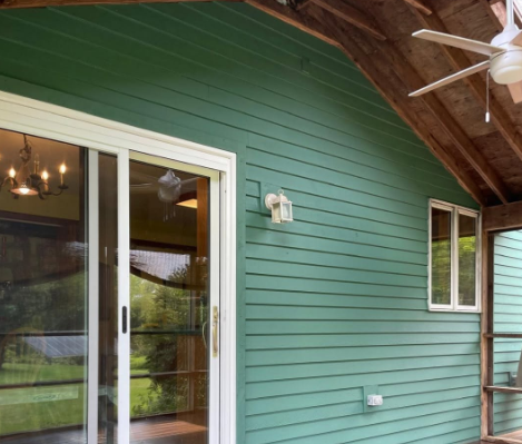 Covered porch with teal siding, sliding glass door, windows, and a ceiling fan under a wood roof.