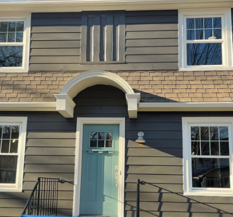 Front entrance of a gray house with a mint-green door and arched white trim, flanked by windows and black railings
