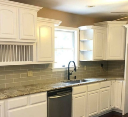 Bright white kitchen with white cabinets, beige tile backsplash, granite counters, and a black dishwasher and faucet