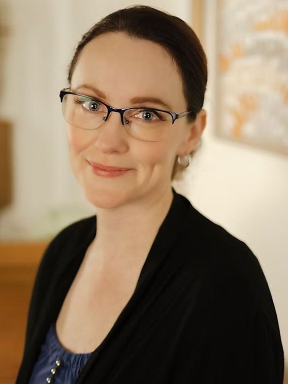 Portrait of a smiling person wearing glasses and a black cardigan over a blue top
