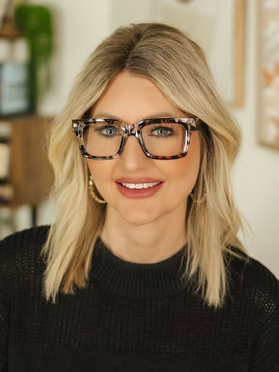 Portrait of a smiling person with blonde hair and glasses, wearing a black sweater indoors