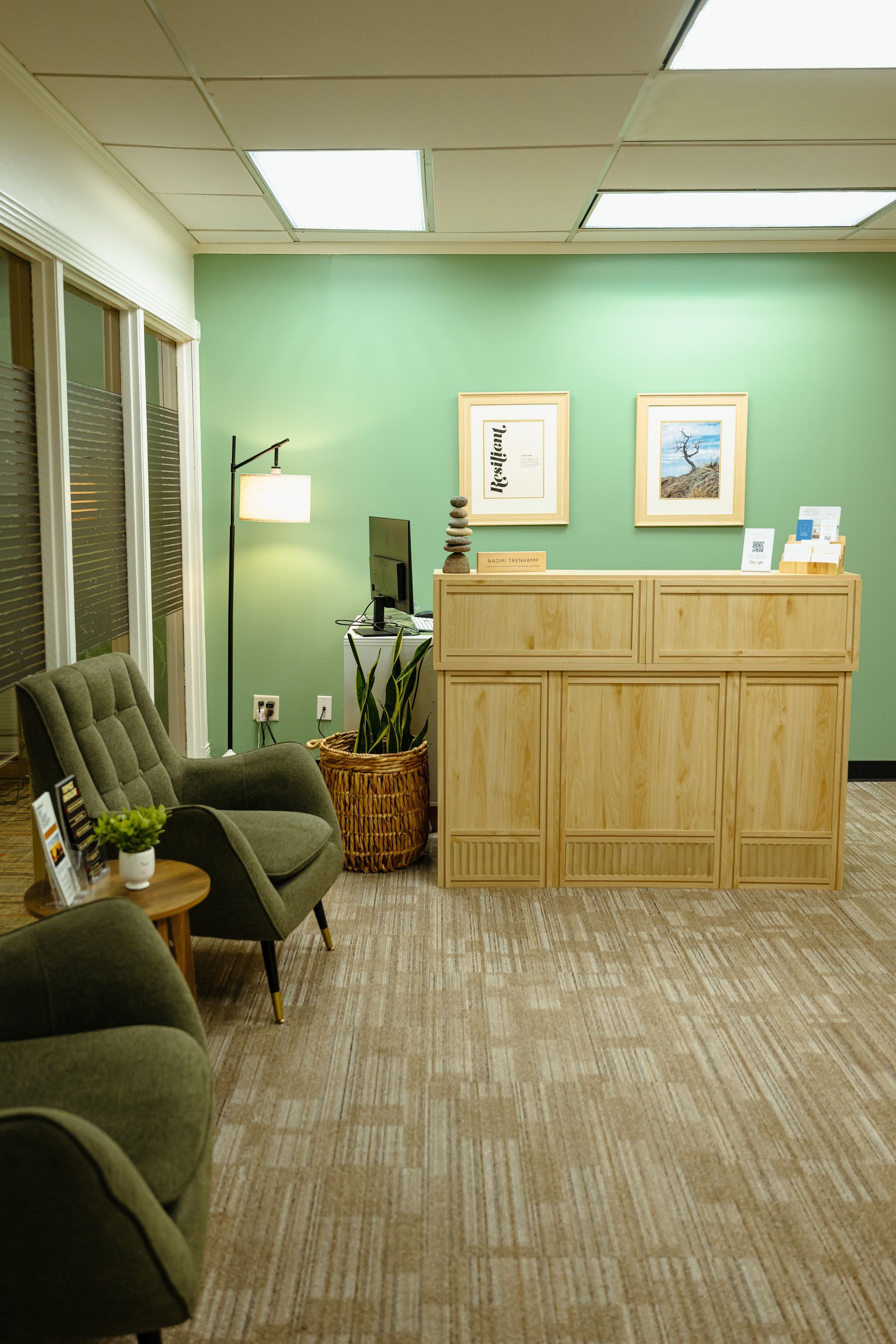 Quiet medical office waiting room with chairs, lamp, and wooden reception desk on mint-green walls