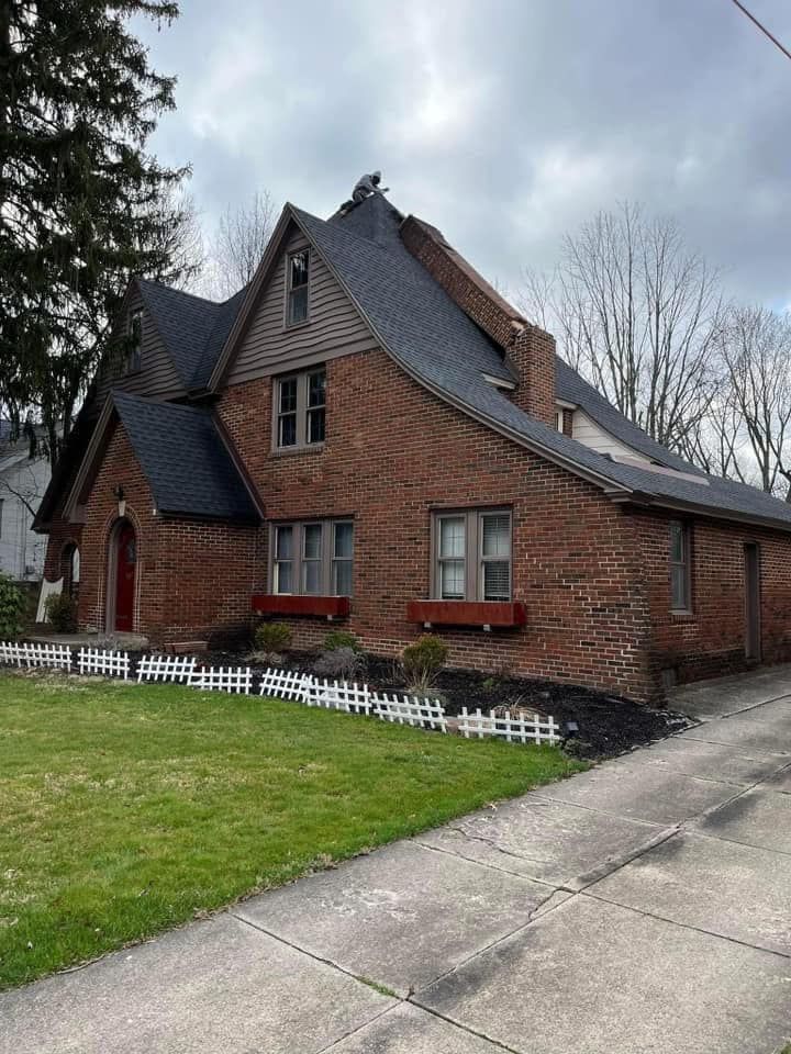 A large brick house with a black roof and a white picket fence.