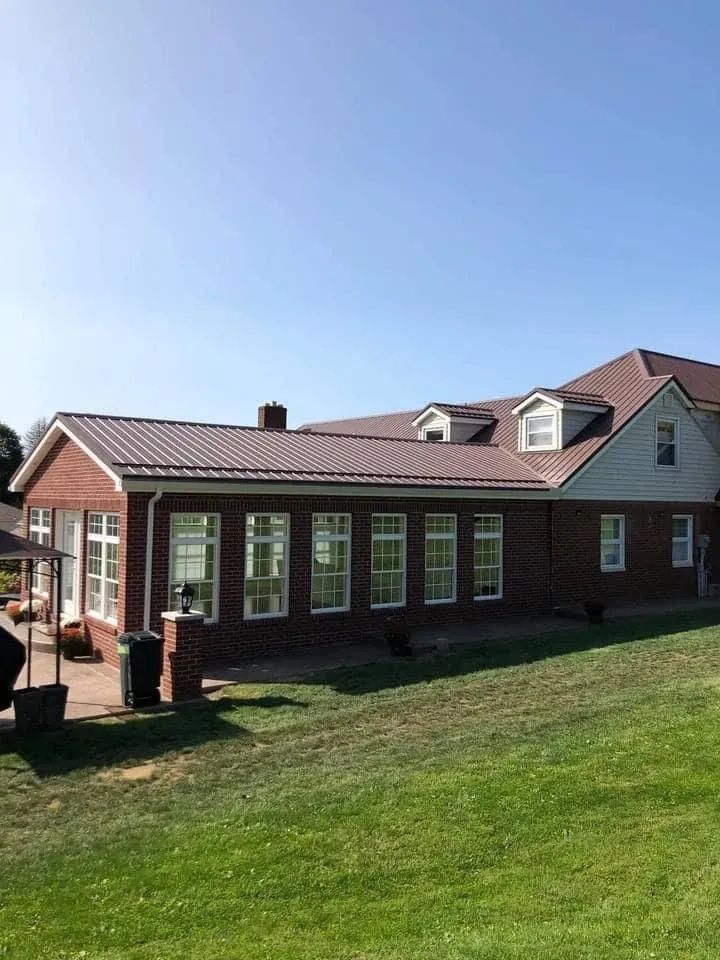 A large brick house with a metal roof is sitting on top of a lush green field.