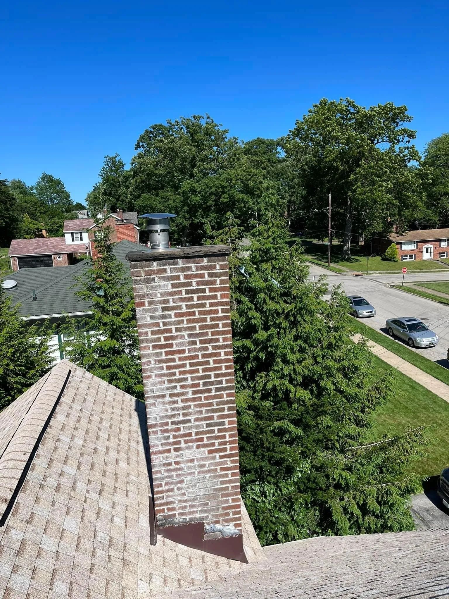 A brick chimney is sitting on top of a roof in a residential area.