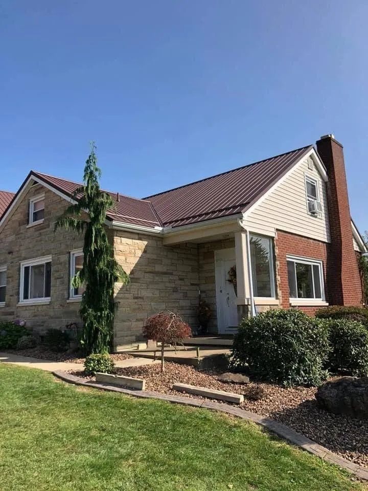 A large brick house with a red roof is sitting on top of a lush green lawn.