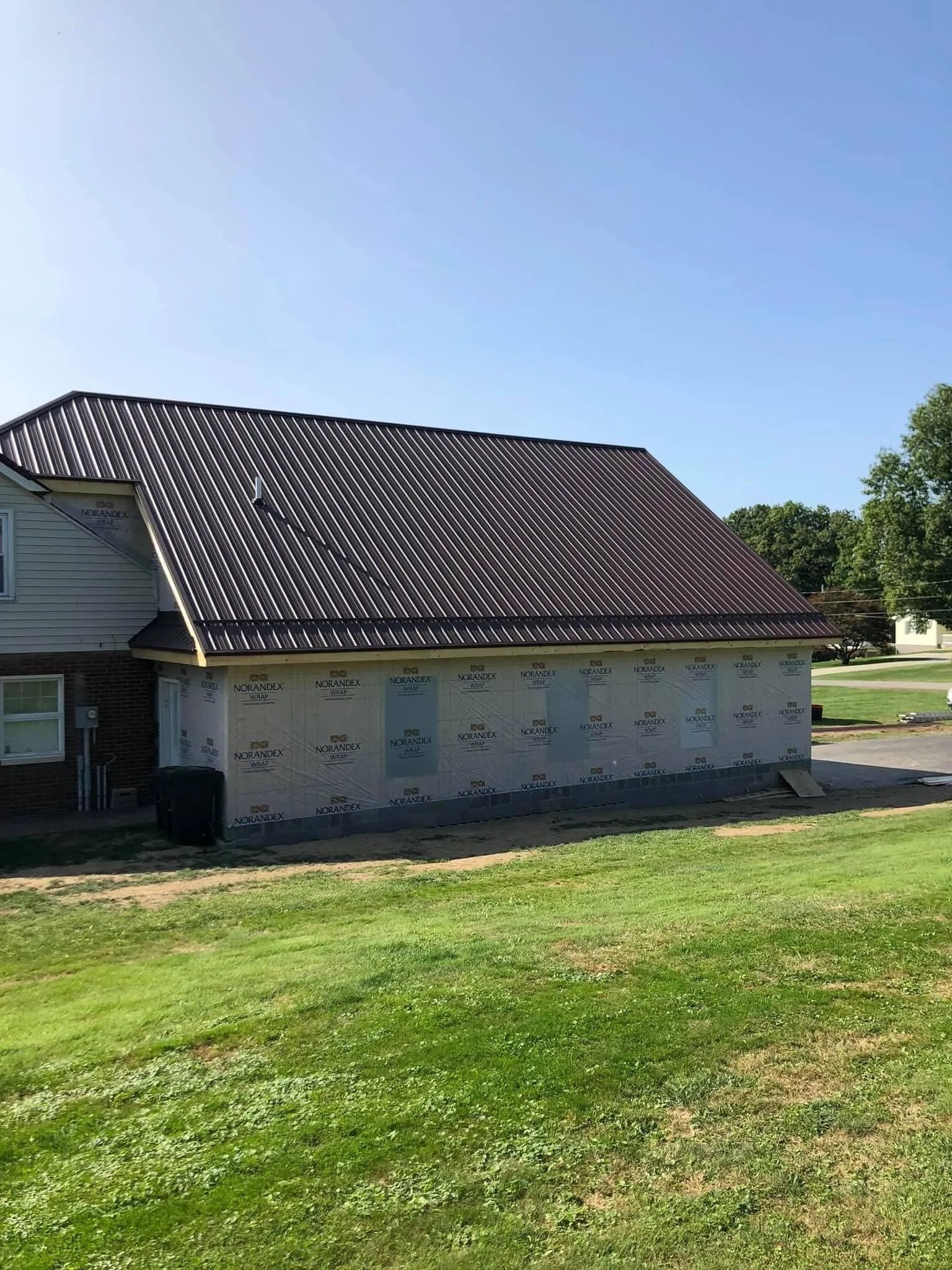 A house with a metal roof is sitting on top of a lush green field.