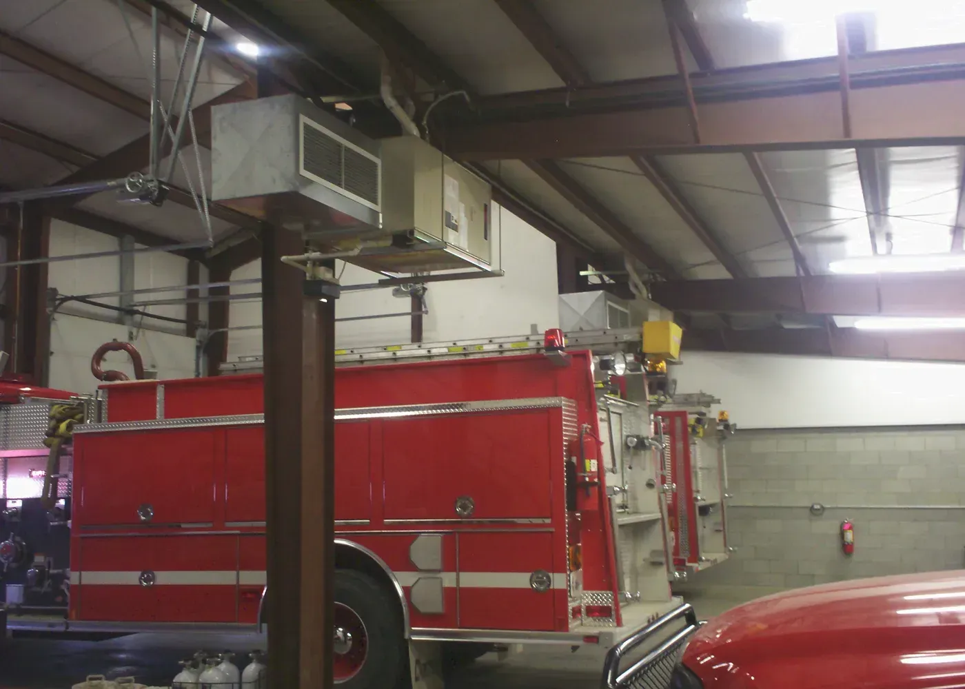 A fire station interior featuring a large red fire truck parked in a bay beneath ceiling-mounted heating units.